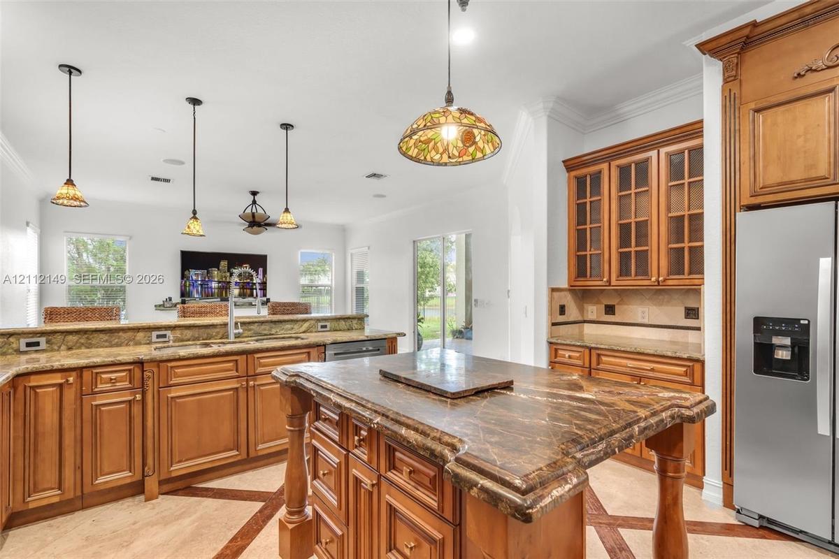 Kitchen featuring wood cabinetry, stone countertops, central island, decorative pendant lighting, and patterned stone flooring