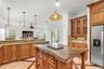 Kitchen featuring wood cabinetry, stone countertops, central island, decorative pendant lighting, and patterned stone flooring