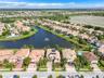 Aerial perspective of a residential community featuring multi-story homes with tile roofs, paved driveways, waterfront access to a central lake, and i