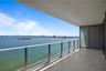 Covered balcony featuring oversized tile flooring, a glass panel railing, and expansive water frontage