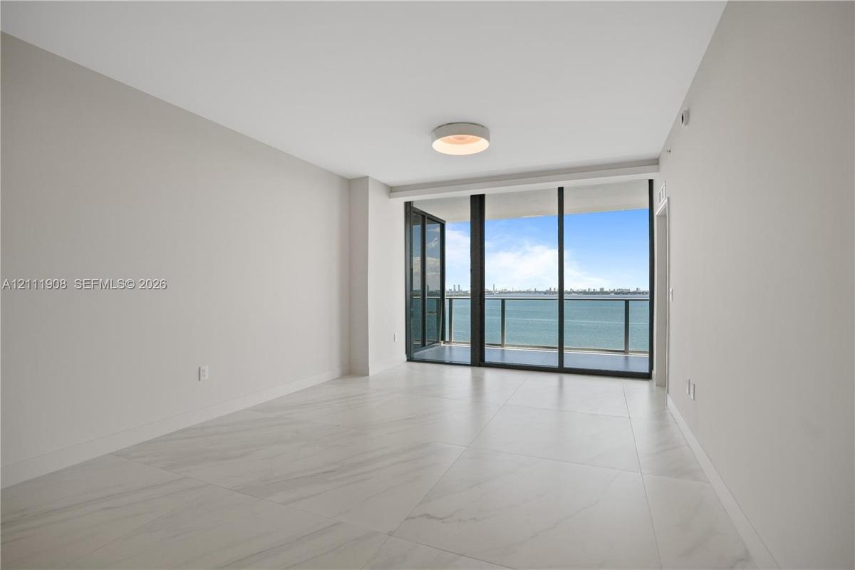 Large-format stone-style flooring, floor-to-ceiling glass paneling, and access to a balcony with a metallic railing