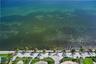 Direct waterfront access with a paved promenade, mature palm trees, manicured lawn, and stone-paver hardscaping