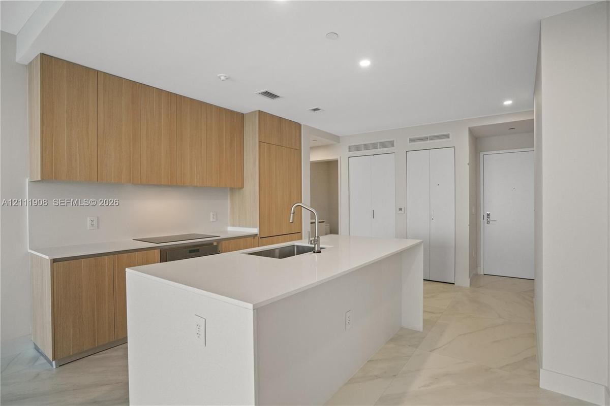 Kitchen featuring flat-panel wood cabinetry, quartz countertops, a central island with an undermount sink, integrated appliances, and large-format til