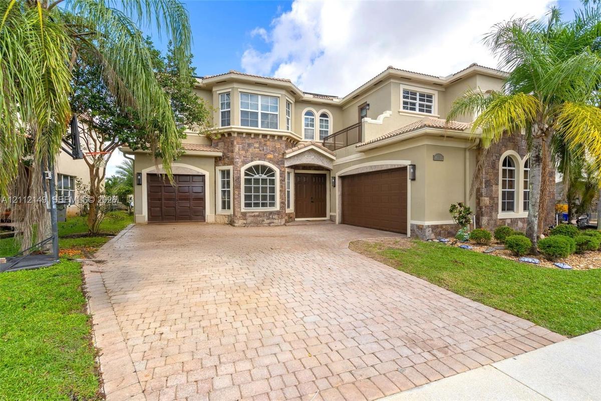 Two-story exterior featuring a stone facade, arched windows, dual garage doors, and a paved driveway