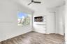Neutral-toned wood-finish flooring, white built-in shelving, ceiling fan, and multi-pane window