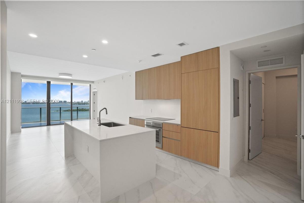 Kitchen featuring an island with a stone countertop, flat-panel wood cabinetry, integrated appliances, recessed lighting, and large-format tile floori