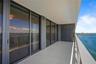 Covered balcony featuring expansive glass sliding doors, tiled flooring, and a metal railing overlooking the water