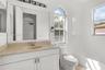 Bathroom featuring a white vanity cabinet, neutral countertop with integrated sink, arched window, and a built-in tub with tile surround