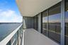 Covered balcony with large-format tile flooring, tempered glass railings, and floor-to-ceiling sliding glass doors