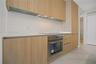 Flat-panel cabinetry with a natural wood finish, integrated stainless steel oven, cooktop, solid-surface countertops, and large-format tile flooring