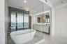 Freestanding soaking tub, glass-enclosed shower, wall-mounted double vanity, backlit mirror, and floor-to-ceiling windows