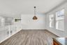 Open space featuring wood-finish flooring, white walls, crown molding, double windows with horizontal blinds, and a suspended geometric pendant light 