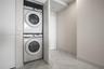 Stacked laundry center with high-capacity washer and dryer, finished with large-format tile flooring and neutral wall paint