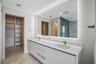Double vanity with a composite countertop and integrated sinks, metallic hardware, full-width illuminated mirror, and custom built-in cabinetry with s