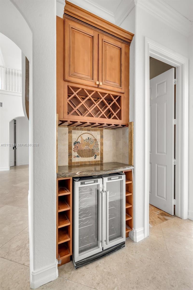 Built-in cabinetry featuring wood-finish wine storage, glass-door beverage refrigeration, a stone-surfaced countertop, and decorative mosaic tile back