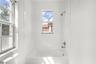 Bathtub and shower combination featuring full-height white wall tile, dual windows, and polished chrome plumbing fixtures