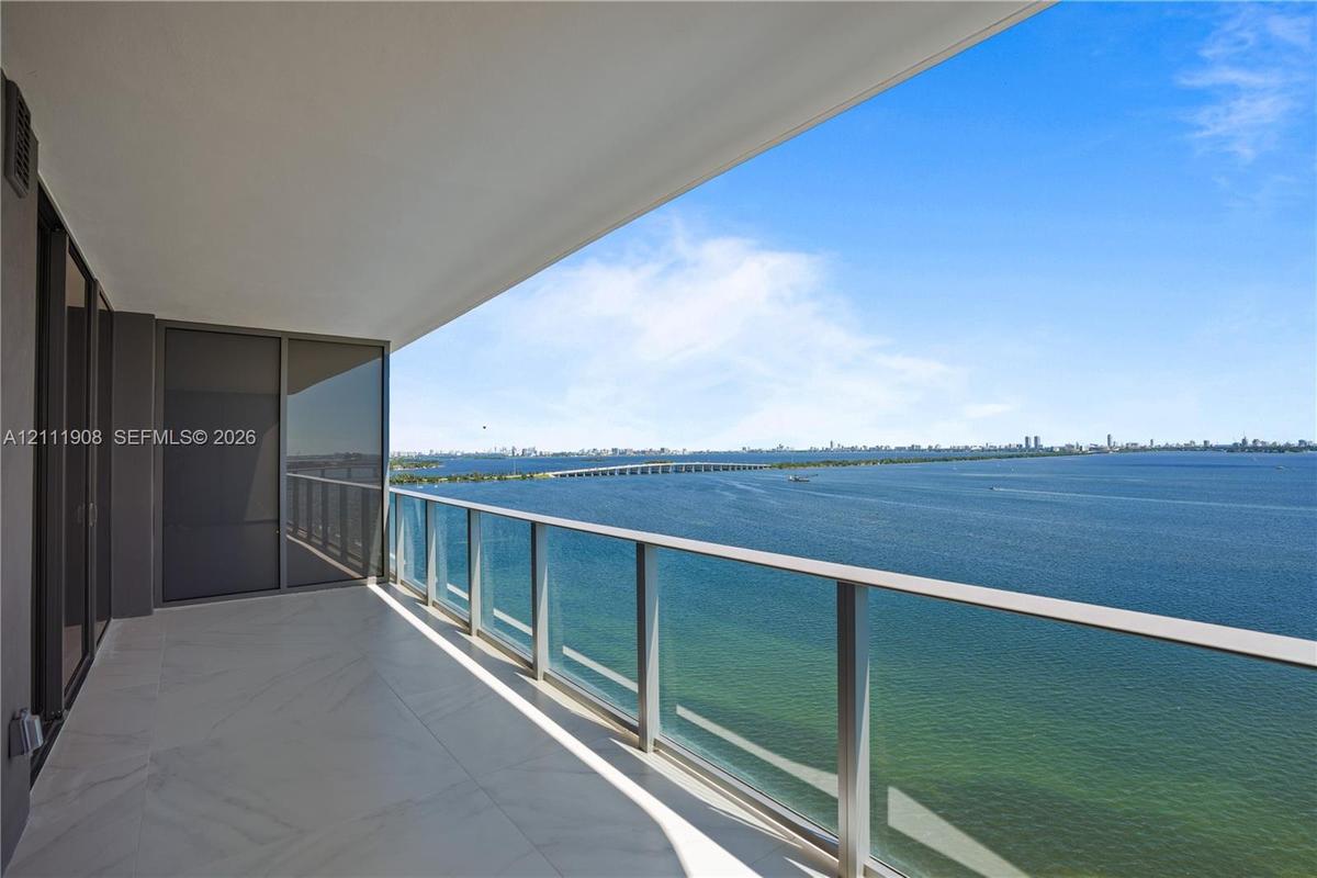 Covered balcony featuring expansive stone tile flooring and floor-to-ceiling glass panel railings