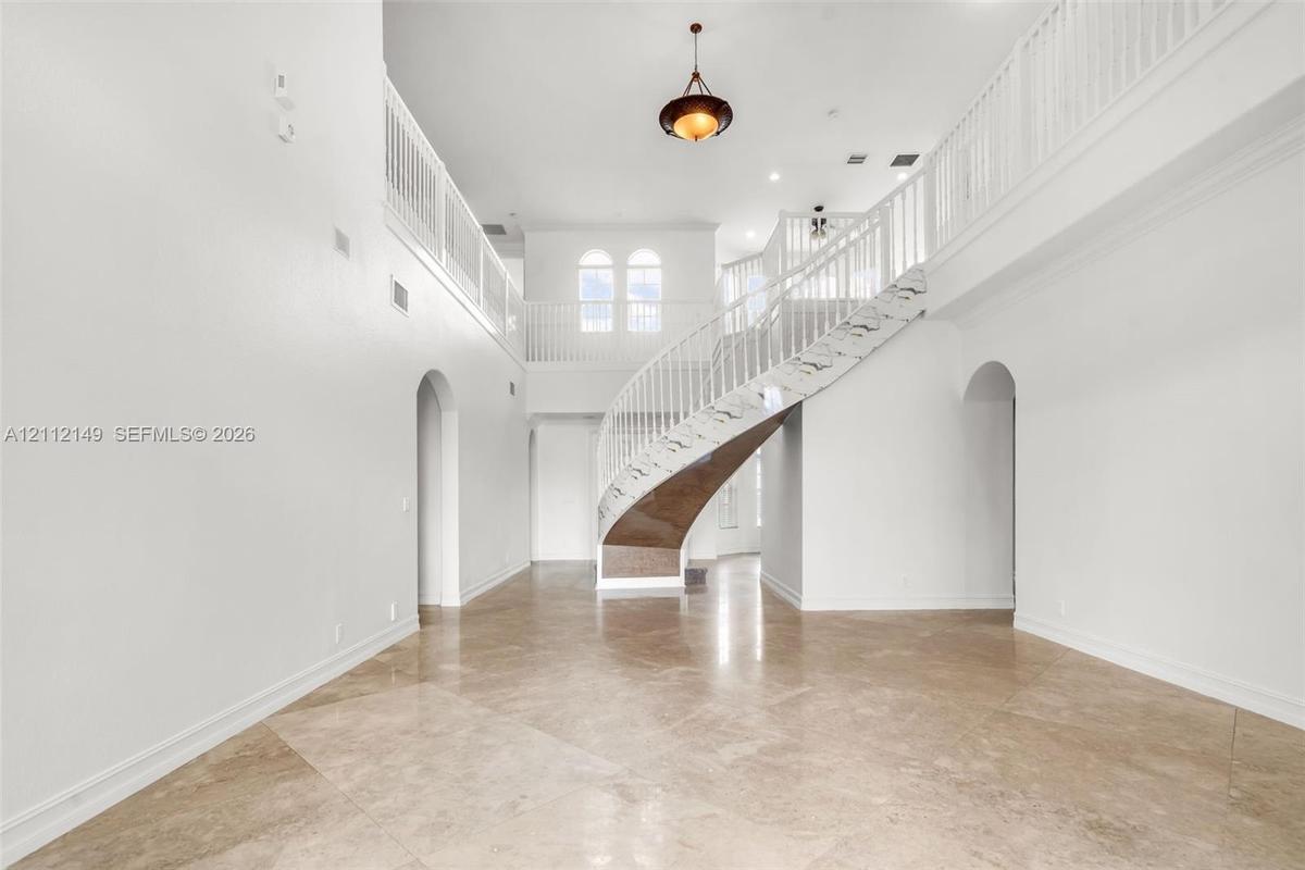 Grand foyer featuring high ceilings, curved staircase with white railings, polished stone flooring, arched entryways, and recessed lighting