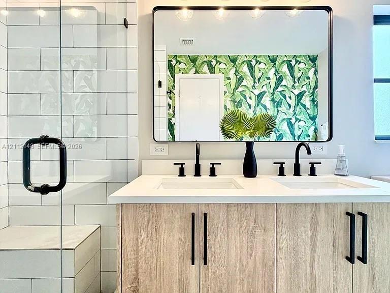 Dual-sink vanity with light-tone wood-finish cabinetry, white countertop, rectangular undermount sinks, and matte black fixtures, paired with a walk-i