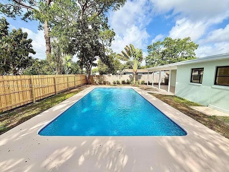 Rectangular in-ground swimming pool featuring a concrete pool deck, enclosed by a wood privacy fence and covered exterior patio area