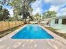 Rectangular in-ground swimming pool featuring a concrete pool deck, enclosed by a wood privacy fence and covered exterior patio area
