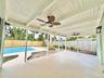 Covered patio featuring a painted wood-beam ceiling, ceiling fans, wall-mounted lanterns, concrete flooring, and an in-ground swimming pool