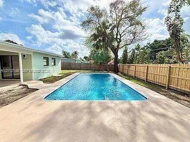 Rectangular in-ground swimming pool with concrete decking, enclosed by wood privacy fencing and mature trees