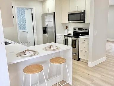 Kitchen featuring white cabinetry, solid-surface countertops, stainless steel appliances, and wood-finish flooring