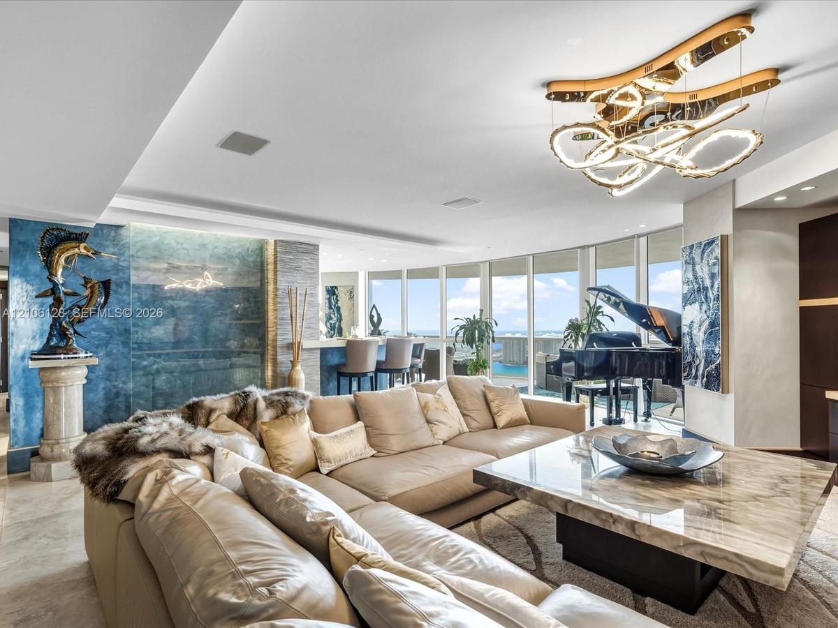 Expansive floor-to-ceiling windows, custom sculptural light fixture, textured blue accent wall, recessed ceiling lighting, and stone flooring
