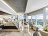 Floor-to-ceiling windows, stone tile flooring, tray ceiling with recessed lighting, wall-mounted fireplace, and elevated platform bed base