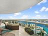 Curved covered balcony featuring stone flooring and a glass railing with metal trim