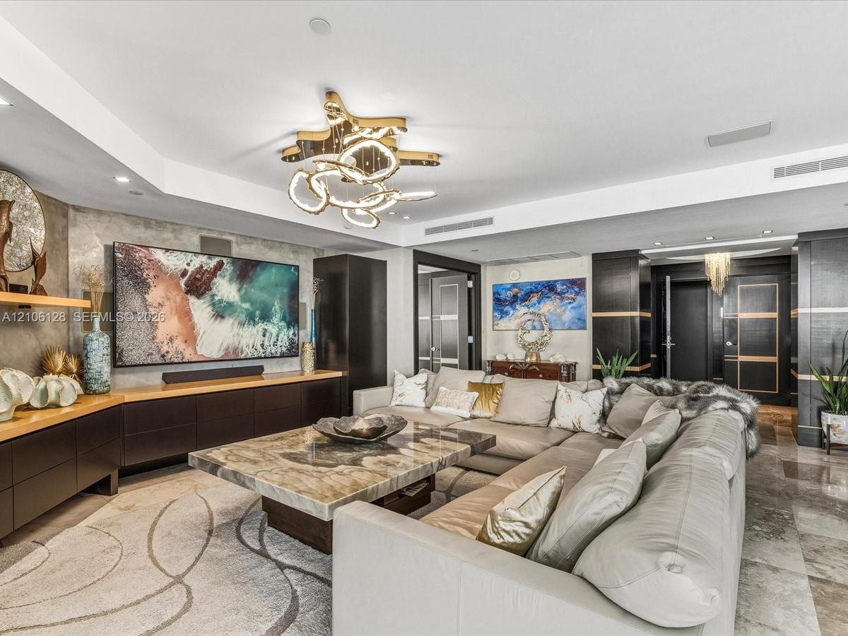 Custom built-in cabinetry with integrated shelving, stone-surfaced center table, polished stone flooring, and multi-tiered contemporary statement ligh