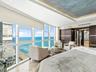 Floor-to-ceiling windows, ocean horizon backdrop, recessed ceiling lighting with painted artistic detail, built-in dark wood cabinetry, and polished s