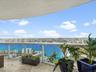 Curved balcony featuring natural stone flooring and a glass railing system, overlooking expansive water and coastal city scenery