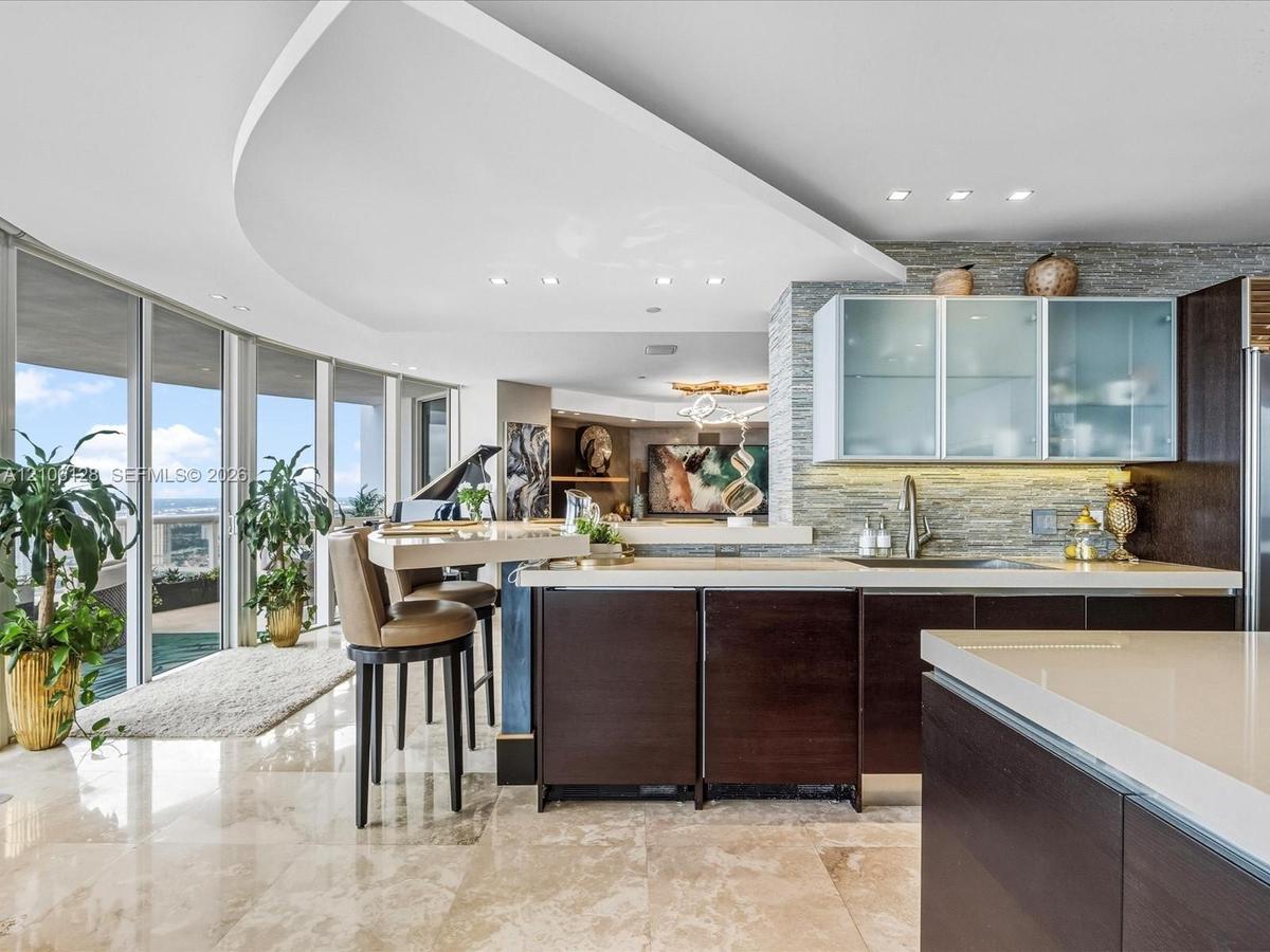 Gourmet kitchen featuring floor-to-ceiling glass walls, custom dark-finish cabinetry, stone-tile flooring, stacked-stone backsplash, and a curved arch