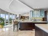 Gourmet kitchen featuring floor-to-ceiling glass walls, custom dark-finish cabinetry, stone-tile flooring, stacked-stone backsplash, and a curved arch