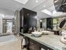 Custom dual-sink vanity featuring stone-surfaced countertops, dark built-in cabinetry, white vessel sinks, and a drop-in soaking tub encased in stone 