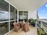 Covered private balcony featuring stone flooring, floor-to-ceiling glass paneling, and glass-and-metal railings
