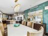 Dining area featuring a custom crystal chandelier, textured teal feature wall, integrated recessed lighting, and a neutral stone-surface table