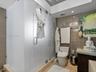Walk-in shower enclosure featuring frosted glass panels, neutral-toned wall tile, modern dual-flush toilet, and stone-surface countertop
