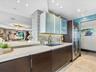 Modern kitchen featuring dark wood-finish cabinetry, frosted glass upper cabinets, a light-toned countertop, a built-in stainless steel refrigerator, 