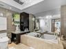 Bathroom featuring a stone-encased jetted soaking tub, dark-finish cabinetry with an integrated countertop, wall-to-wall mirror, tiled walls, and a cr