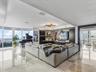 Open-concept interior featuring floor-to-ceiling windows, polished stone flooring, custom dark wood built-in cabinetry, and a tiered modern chandelier