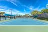 Hard-court tennis facility featuring blue and green surface markings, perimeter privacy fencing, overhead lighting, and built-in shaded seating areas