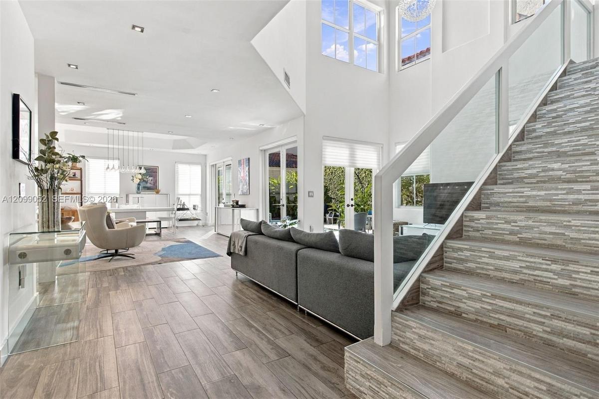 Double-height ceiling, glass-paneled staircase railing, stacked stone-texture stair risers, wood-finish flooring, and multiple sets of French doors