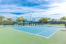 Hard-surface tennis courts featuring perimeter mesh fencing, blue sunshades, integrated court lighting, and mature landscaping