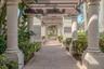 Outdoor walkway featuring a brick-paver path, structural stone columns, overhead timber-frame pergola, and integrated wall-mounted lantern lighting