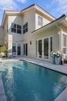 Stucco exterior with a tiled roof, featuring multiple sets of white-framed glass paneled doors and a private swimming pool with stone paver decking