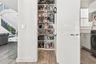 Walk-in pantry featuring floor-to-ceiling custom white shelving, high-gloss flat-panel door, and wood-finish flooring