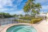 In-ground spa with stone-tiled interior, paver patio, decorative metal perimeter fencing, and mature palm trees